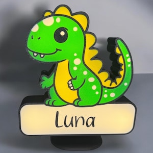 May include: A green and yellow dinosaur night light with white spots. The dinosaur is holding a sign that says "Luna".