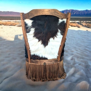 Elevate your farmhouse decor with this stunning Western Style Brown Leather Chair, a perfect blend of rustic charm and vintage appeal. Crafted from reclaimed wood and upcycled materials, this unique piece features a distressed brown leather frame that exudes cowboy cool. The upholstery is adorned with a striking Highland cow print, adding a touch of countryside authenticity, while the goat-skin hides drape gracefully over the seat, offering both comfort and texture.