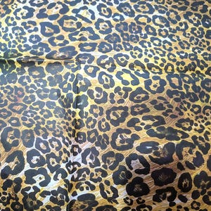 May include: A fabric with a leopard print pattern. The design features black spots on a tan and brown background. The fabric is folded, creating a textured appearance. The overall theme is animal print.