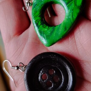 May include: A pair of earrings, one is a green triangle with a circle cutout, the other is a black button with four holes.
