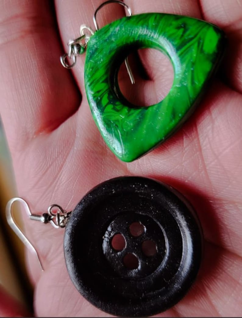 May include: A pair of earrings, one is a green triangle with a circle cutout, the other is a black button with four holes.