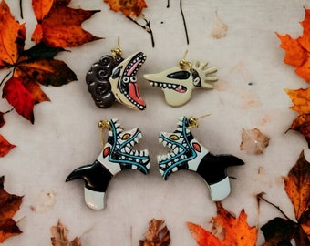 May include: Four dangle earrings featuring character designs. The top left is a dark brown creature with a wide mouth, the top right is a pale ghost dog, and the bottom two are identical black and white creatures with sharp teeth and blue accents.
