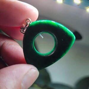 May include: A green jade pendant with a circular hole in the center. The pendant is shaped like a teardrop and has a silver bail.
