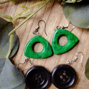 May include: A pair of earrings with green triangle-shaped pendants with a swirl pattern and black button-shaped pendants.