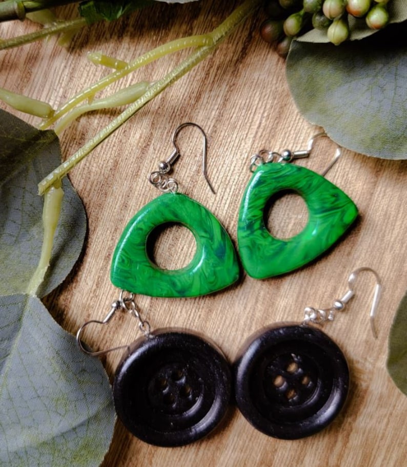 May include: A pair of earrings with green triangle-shaped pendants with a swirl pattern and black button-shaped pendants.