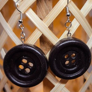 May include: A pair of black button earrings with silver hooks. The buttons have four holes each.