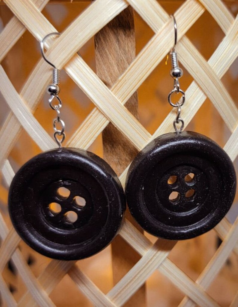 May include: A pair of black button earrings with silver hooks. The buttons have four holes each.