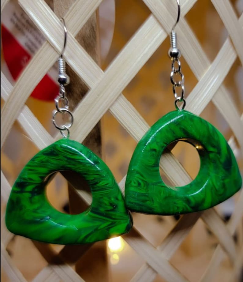 May include: A pair of green triangle-shaped earrings with a swirl pattern and a circular opening in the center. The earrings are made of polymer clay and have silver hooks.