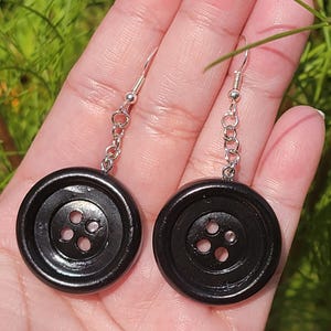May include: A pair of black button earrings with silver chains. The buttons have four holes.