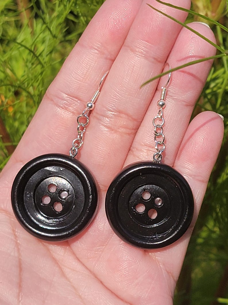 May include: A pair of black button earrings with silver chains. The buttons have four holes.