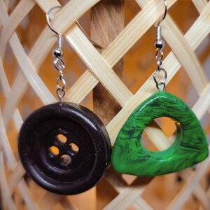 May include: A pair of earrings with a black button and a green triangle pendant. The button has four holes and the triangle has a hole in the center.