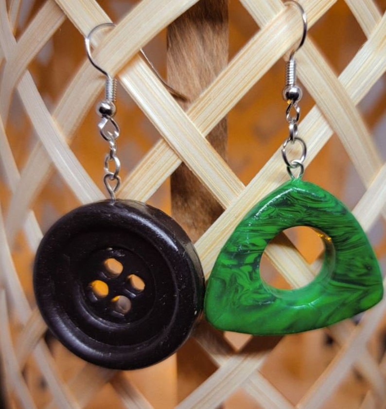 May include: A pair of earrings with a black button and a green triangle pendant. The button has four holes and the triangle has a hole in the center.