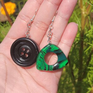 May include: A pair of earrings featuring a black button and a green and black marbled triangle pendant.