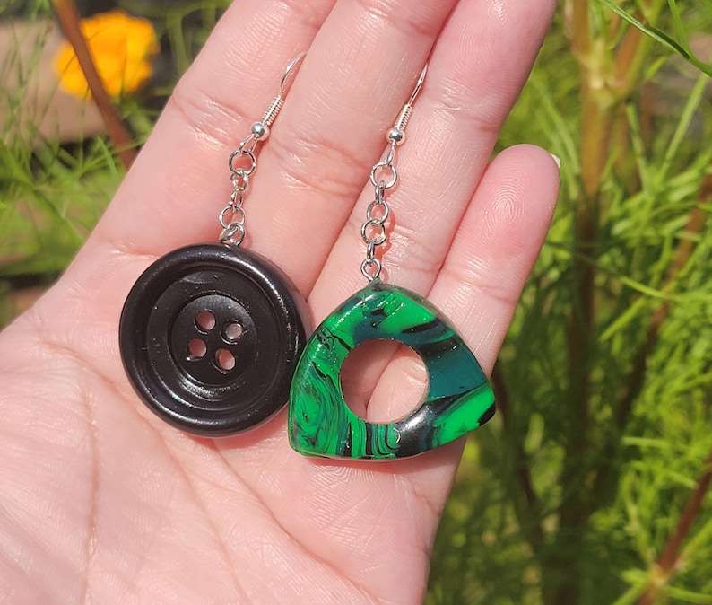 May include: A pair of earrings featuring a black button and a green and black marbled triangle pendant.