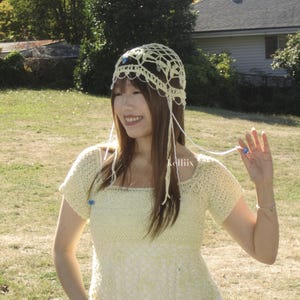 May include: A light yellow crochet top and matching head covering with dangling strands. The top has short sleeves and a square neckline. The head covering is adorned with small blue beads. The word "kelliiix" is visible on the top.