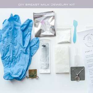 May include: A DIY breast milk jewelry kit with a blue pair of gloves, a silver pouch with two clear vials, a white powder, a blue spatula, a clear syringe, a white pad, a clear vial, a silver pendant, a silver chain, and instructions for making jewelry.