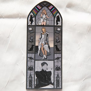 May include: A stained glass artwork depicting a woman in a white outfit, with black and white illustrations of typewriters, dogs, and other figures. The artwork is in a gothic arch shape and has a grey and white colour scheme.
