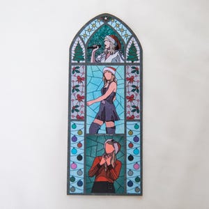 May include: A stained-glass style artwork featuring three panels of a person wearing a Santa hat. The top panel shows the person singing into a microphone. The middle panel shows the person in a dress. The bottom panel shows the person with their hands clasped.