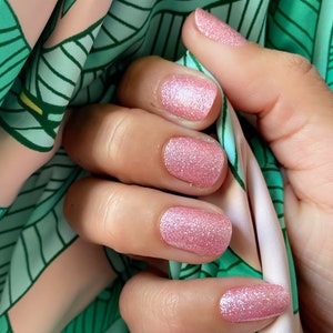 May include: Close-up of a hand with five fingernails painted with a light pink glitter nail polish.