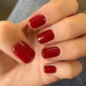 May include: Close-up of five fingernails painted with a bright red nail polish.