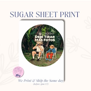 May include: A sugar sheet print featuring a circular image with the text "BAD BUNNY DEBI TIRAR MAS FOTOS". The image shows two cartoon characters sitting in chairs, one taking a photo. The text "SUGAR SHEET PRINT" is at the top.