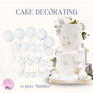 Könnte beinhalten: Bild von Tortendekorationszubehör. Es zeigt weiße, blasenartige Dekorationen auf Drahtstielen und eine zweistöckige Torte mit goldenen Akzenten. Der Text "CAKE DECORATING" und "20 piece 'Bubbles'" ist enthalten.