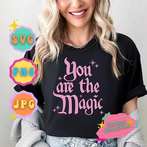May include: A black t-shirt with the text "You are the Magic" in pink script. The text is surrounded by small white stars. The shirt is being worn by a person with long blonde hair.