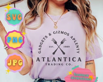 Puede incluir: Una camiseta morada con un logotipo en blanco y negro que dice "Gadgets & Gizmos Aplenty Est. 1989 Atlantica Trading Co."