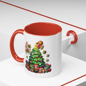 Puede incluir: Una taza de cerámica blanca con un borde y un asa rojos. La taza presenta un árbol de Navidad con regalos y un hombre de jengibre en la parte superior. La taza está sobre una superficie blanca.