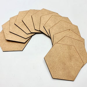 Op de afbeelding: Een verzameling van elf onafgewerkte, lichtbruine, zeshoekige houten uitsparingen, gerangschikt in een gebogen patroon. De uitsparingen zijn gemaakt van een glad, uniform materiaal en zijn geschikt voor diverse knutselprojecten. De neutrale kleur en geometrische vorm bieden veelzijdigheid.