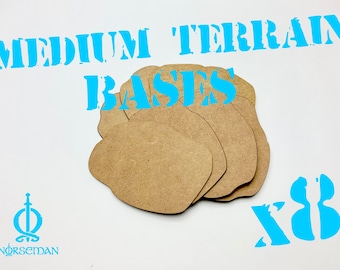 Op de afbeelding: Een stapel van acht middelgrote terreinbases van lichtbruin materiaal. De bases hebben een onregelmatige vorm. De woorden "MEDIUM TERRAIN BASES" zijn in het blauw geschreven. Het nummer "x8" is ook in het blauw.
