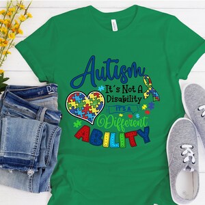 May include: Green t-shirt with a blue and rainbow puzzle piece heart and the text "Autism It's Not A Disability It's A Different Ability".