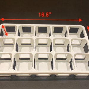 May include: A white plastic tray with 15 square compartments. The tray is 16.5 inches long, 10 inches wide, and 2.5 inches deep. The compartments are open at the top and have a square opening.