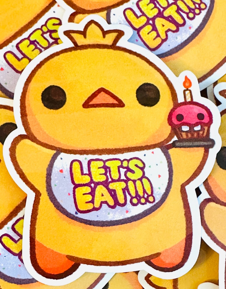 May include: A yellow chick with a crown and a bib that says "Let's Eat!!" is holding a pink cupcake with a lit candle. The chick has big black eyes and a small orange beak.