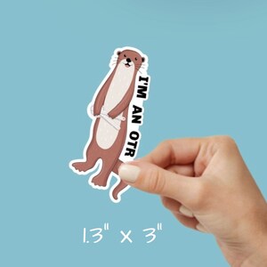 Peut inclure: Un autocollant repr&eacute;sentant une loutre brune et blanche avec le texte "I'm an OTR" sur un fond bleu. L'autocollant mesure 1,3 pouce par 3 pouces.