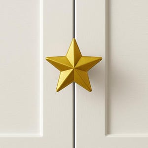 Könnte beinhalten: Nahaufnahme eines weißen Schranks mit einem goldfarbenen sternförmigen Griff. Der Griff ist mittig auf den Schranktüren angebracht und bietet ein dekoratives und funktionales Element. Der Stern-Griff verleiht dem Schrank einen Hauch von Laune.