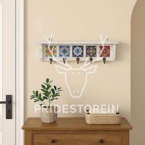 May include: A white wooden wall-mounted coat rack featuring five decorative tiles with colourful geometric and floral patterns. The rack includes five metal hooks for hanging items and a small top shelf. The tiles display blue, yellow, red, and black designs.