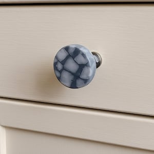 以下が含まれることがあります： グレーと白の色合いのモザイク模様のキャビネットノブのクローズアップ。ノブは丸く、薄いベージュのキャビネットドアに取り付けられています。金具はシルバーです。