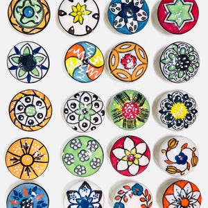 Puede incluir: Colección de 30 pomos de cerámica decorativos para armarios. Cada pomo presenta un diseño floral único pintado a mano en varios colores, incluyendo azul, naranja, verde y rojo. Los pomos son redondos y tienen un acabado brillante.