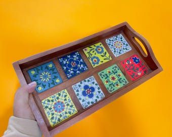 May include: Wooden serving tray with eight square, colorful tiles. Each tile features a different floral design in shades of blue, yellow, green, and red. The tray has a dark brown frame and a handle on each side.