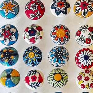 Puede incluir: Surtido de 16 pomos de cerámica con varios patrones florales y geométricos coloridos. Los pomos son redondos y tienen una base blanca.