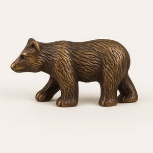 Può includere: Una statuetta di un orso in bronzo con una superficie dettagliata e testurizzata. L'orso cammina con la testa girata di lato.