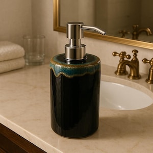 May include: A black ceramic soap dispenser with a stainless steel pump. The top of the dispenser has a turquoise and brown glaze. The dispenser is cylindrical and sits on a marble countertop.