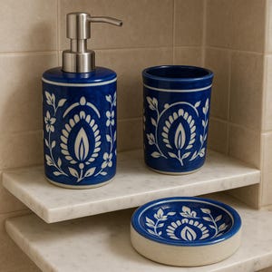 May include: A blue and white ceramic bathroom set featuring a floral design. The set comprises a soap dispenser with a silver pump, a tumbler, and a soap dish. The pieces are decorated with a white floral pattern.