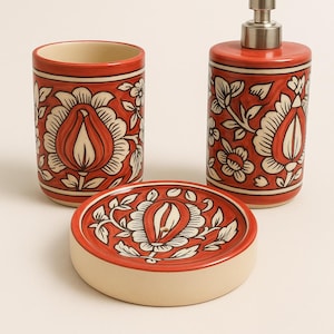 Könnte beinhalten: Ein dreiteiliges Badezimmer-Set mit einem roten und cremefarbenen Blumenmuster. Das Set umfasst einen Becher, einen Seifenspender mit silberner Pumpe und eine Seifenschale. Die Teile sind aus Keramik.