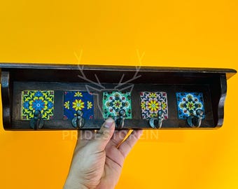 May include: Wooden wall-mounted coat rack with five decorative ceramic tiles. Each tile features a unique floral pattern in vibrant colors. The rack has five metal hooks for hanging items. The text "PRIDESTOREIN" is visible.