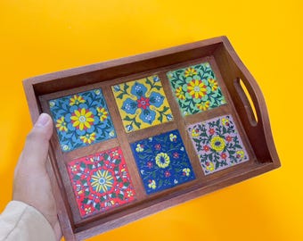 May include: Wooden serving tray with six square, colorful floral tile inserts. The tiles feature yellow, blue, red, and green floral patterns. The tray has a dark brown finish and integrated handles.