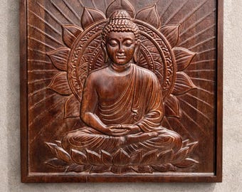 May include: A square dark brown wooden wall plaque featuring a relief carving of a seated figure in a meditative pose. The figure is centered on a large lotus flower with radiating sunburst lines extending to the edges of the wooden frame.