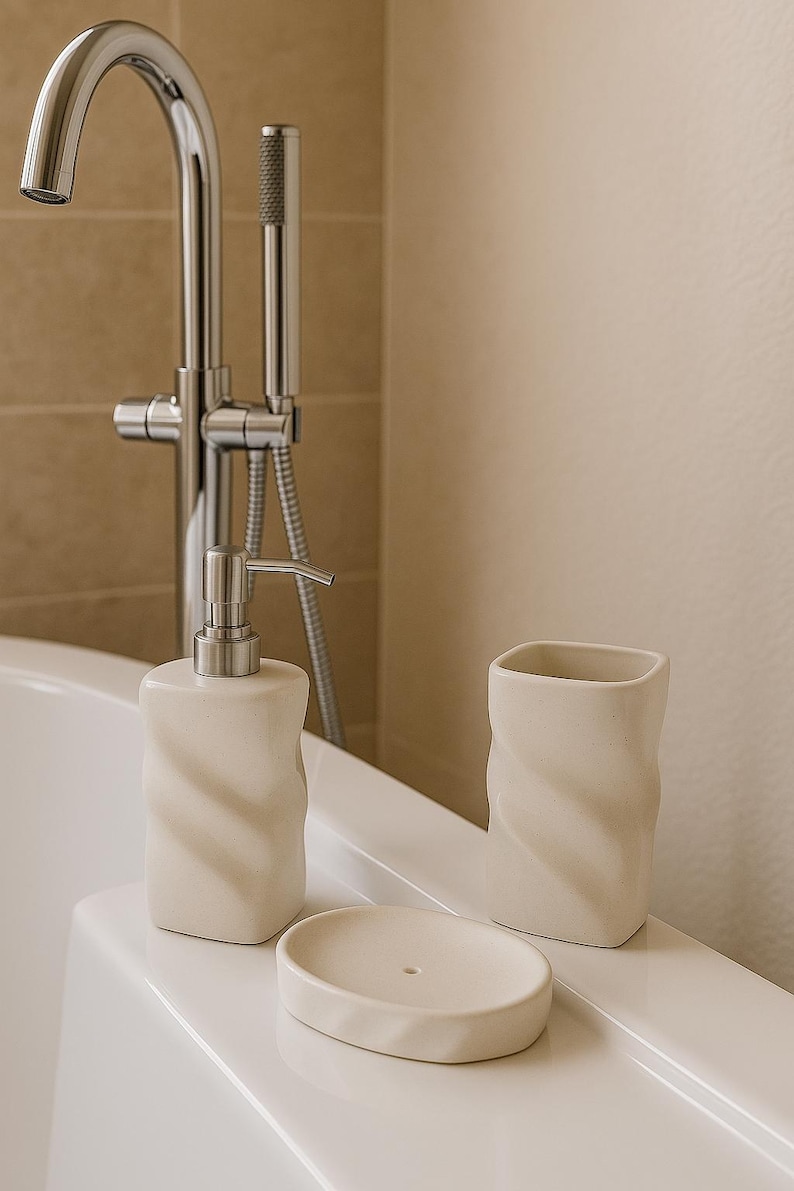 May include: A cream-colored bathroom set featuring a soap dispenser, a tumbler, and a soap dish. The ceramic pieces have a twisted design. A chrome faucet and showerhead are in the background.