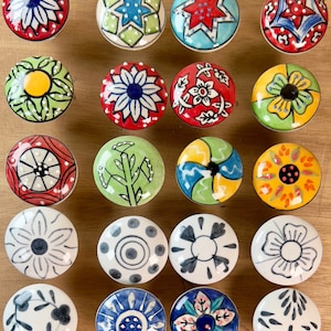 May include: Assortment of 16 colourful ceramic drawer knobs with various floral, geometric and abstract designs. The knobs are round and have a glossy finish.